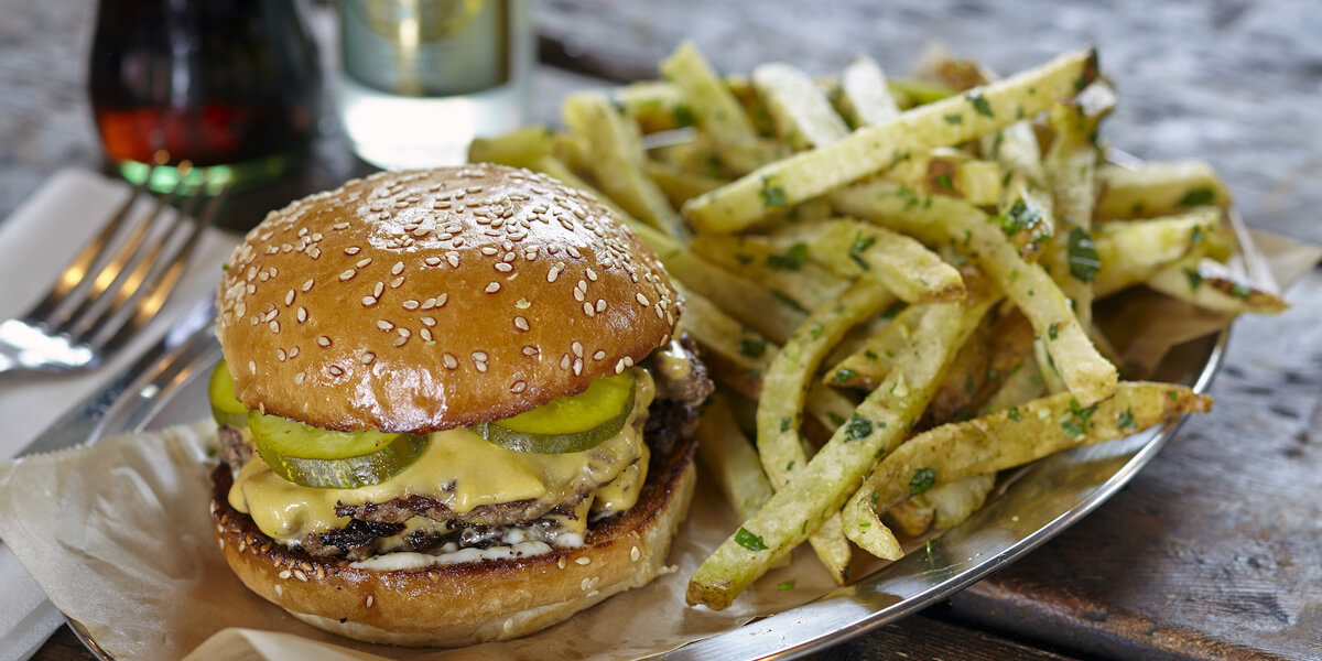 A plate of cheeseburger with pickles with a side of fries